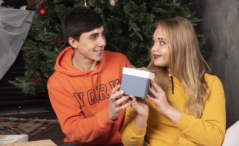 A young couple exchanging a heartfelt gift in front of a decorated Christmas tree, symbolizing meaningful gifts for him.