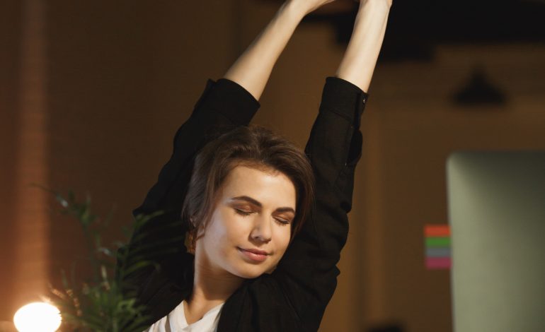 A woman stretching at her desk with a relaxed expression, showing how short breaks can help you Stay Motivate and productive