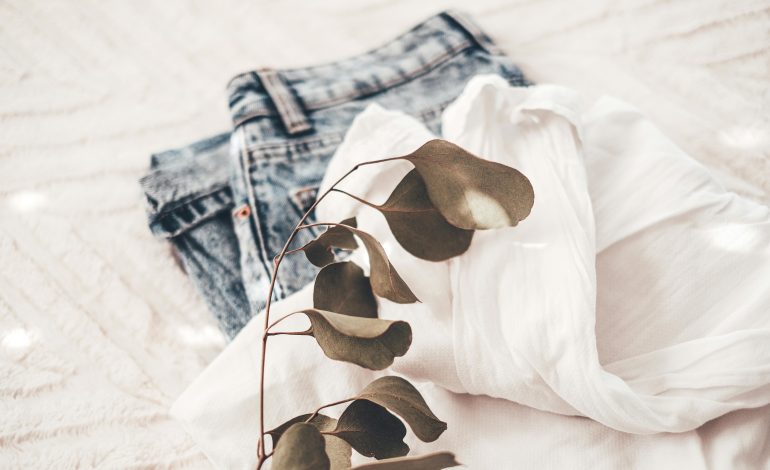 A stylish white blouse and denim jeans laid on a soft surface, representing classic wardrobe essentials.